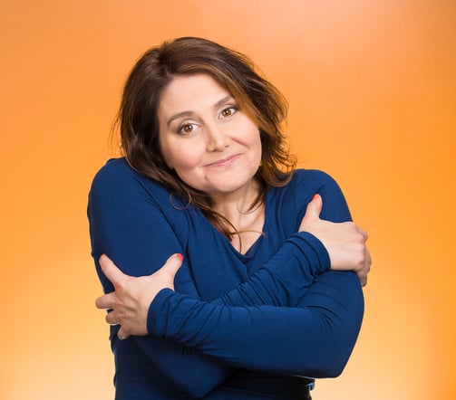 Closeup portrait happy smiling woman, holding, hugging herself, isolated orange background. Positive human emotion, facial expression, feeling, reaction, situation attitude. Life love yourself concept